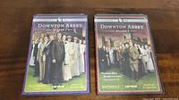 Two DVD cases showing Downton Abbey Seasons 1 and 2 placed side by side on wooden surface