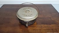 Side view of black cast iron Dutch oven with silver lid and wire handle on wooden surface.