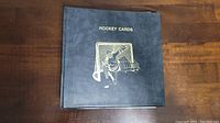 Closed black hockey card binder with gold embossed hockey goalie graphic on front cover, labeled 'Hockey Cards'.