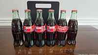 Six glass Coca-Cola bottles featuring different label designs on a wooden surface