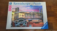 Closed box of Ravensburger 1000-piece puzzle showing New York City image with Brooklyn Bridge, city skyline at sunset, and view from inside vintage convertible car.