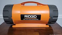 Side view of the RIDGID job site air filtration unit showing its orange cylindrical design with a built-in handle on top and RIDGID branding.
