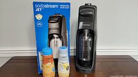 Sodastream Jet machine, packaging box, and two drink mixes on table