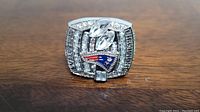 Top view of a wide replica ring with clear stones and embroidered New England Patriots logo