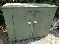 Front view of antique green pine jam cupboard with two slab doors and white porcelain knobs, showing aged paint and square nails.