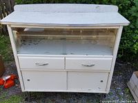 Front view of vintage sideboard showing white formica top and backsplash, glass sliding doors with etched pattern, two drawers with chrome handles, and lower cabinet with sliding doors.