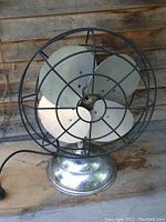 Front view of vintage 1950s nickel-plated mid-century modern table fan showing three blades and wire cage.