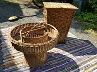 Two large wicker baskets shown outdoors: a tall rectangular hamper with hinged lid, and a round Victorian style flower holder with handle