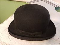 Front and side view of black felt bowler hat showing rounded crown, curled brim and black ribbon band