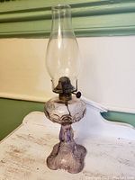 Full front view of antique amethyst oil lamp showing chimney, burner, and patterned glass base