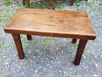 Full view of the antique solid oak footstool taken outdoors on gravel ground showing the top and legs