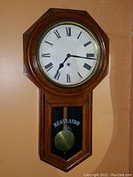 Front view of regulator wall clock showing octagonal wooden case, white Roman numeral dial, brass bezel.