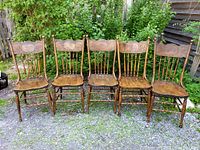 Front view of all five oak pressback spindle chairs on gravel surface