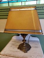Full front view of the early 1920s brass tri-lite table lamp showing the round base and rectangular fabric shade with gold and brown trim.