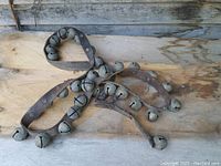 Full view of the large string of metal horse bells on a leather strap placed on wooden surface.