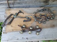 Overview of three old horse bell leather straps laid on wooden surface, showing varying number and condition of bells.