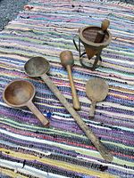 Photo of five wooden utensils (ladles, masher, pats) arranged on a striped rug.
