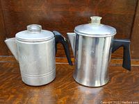 Front view of the pair of aluminum coffee percolators with black handles and clear knobs on lids.