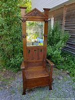 Full front view of oak hall tree outdoors on gravel, showing carved pediment, mirror, bench, and side umbrella ring