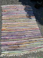 Full view of the multicolored rag rug on ground showing length and color variation with white fringes on edges.