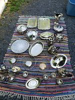 Overview of the vintage silverplate pieces displayed on a striped rug, showing various trays, bowls, teapots, and other serving pieces arranged for visual inventory.