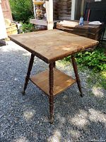 Full side angle view of the vintage square oak table showing top, legs, and lower shelf on gravel surface outside.