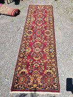 Full view of vintage red runner rug with floral and geometric patterns outdoors on gravel surface.