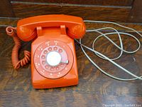 Front view of orange rotary telephone showing dial and coiled cord