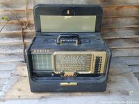 Front view of black Zenith Trans Oceanic radio in open case with handle visible, showing tuning dial and control knobs.