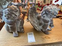 Two baby angel sculptures placed on a wooden surface, showing overall front and side views with visible dust and wear.