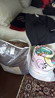 King size brown comforter in packaging, black child's suit jacket, folded bedding items, and sunglasses on sofa.