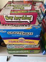 Photo of stacked board games showing Say Anything, Gravity Maze, Huli Babaloo, Pictureka!, and Cranium boxes