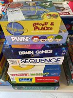 Stack of assorted board games visible from the top, showing titles People & Places, PWNS, Brain Games, Sequence, Who Wants, Family Challenges, and Dimension.