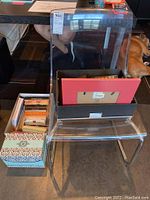 Clear acrylic chair with assorted stationery and boxes on and next to it
