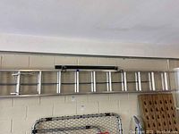 Full view of the 12-foot aluminum extension ladder hanging horizontally against a painted cinder block wall.