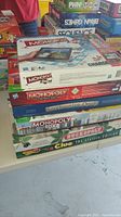 Stack of multiple Monopoly board game boxes and other family games showing diverse editions and designs