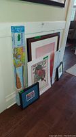 Framed and unframed prints leaning against the wall including Norman Rockwell floral print and boxed US puzzle map.