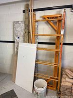 Orange metal scaffolding parts stacked against wall with assorted scrap wood and bucket