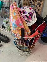 Wire basket containing floral-patterned sports bag, a pink and white bicycle helmet, and other assorted sports gear in a garage setting.