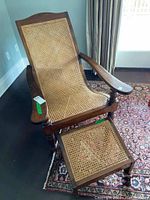 Full view of the wicker chaise lounge chair with footstool on patterned rug.