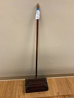 Full front view of carpet sweeper standing upright showing wooden handle and base.