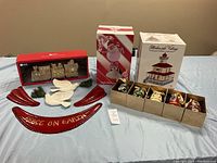 Full lot view showing boxed Christmas village decor, 5 boxed egg ornaments, 3 red 'Peace on Earth' curved decor pieces, and 2 white dove-shaped ornaments