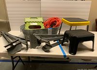 Full view of all items including saw horse legs, step stools, extension cord, and metal bin on table.