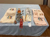 Wide shot showing entire lot on table: towels, metal bowls, cat figurines, journals, bookmarks, keychain.