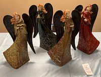 Four ceramic Christmas angels with metal wings arranged together on table, showing color variations and details.