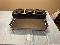Overall shot of the Crockpot party server unit with three ceramic warming pots and the separate rectangular griddle in front