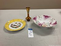 Lot showing a yellow decorative German plate with bird motif, amber hand painted vase with gold detail, and a large hand painted floral bowl with purple color accents.