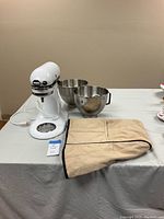 Photo showing white KitchenAid Classic Plus mixer base, two stainless steel bowls, and tan fabric cover on table.
