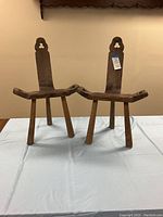 Front view showing both vintage wooden birthing chairs with tripod legs and cut-out decorative shapes on backrests.