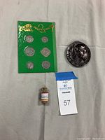 Grouped photo of six Iraqi coins on green card, 1987 Babylon medallion, and small corked vial of brick remains from Jericho.